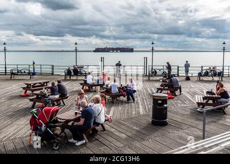 HMM Hamburg am Southend Pier in der Themse-Mündung vorbei, nachdem er den DP World London Gateway Hafen in Essex, Großbritannien, verlassen hat. Leute an Tischen am Pier Stockfoto