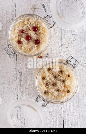 Zwei offene Gläser voll hausgemachten fermentierten Kohl mit Preiselbeeren und schwarzem Pfeffer auf alten weißen Holztischplatten. Flat Lay wi Stockfoto