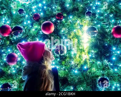 Die Neujahrsbälle auf den Zweigen des Weihnachtsbaums mit einer Girlande und einem Mädchen, das daneben steht, spiegeln sich im Ball wider. Stockfoto