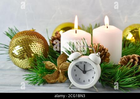 Weihnachtskomposition. Zwei Kerzen und Kiefernzweige mit Zapfen und einem weißen Wecker. Stockfoto