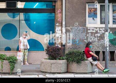 BELGRAD, SERBIEN - 21. AUGUST 2020: Zwei Personen, ein junger Mann und eine alte Frau, warten auf ihren Bus an einer Haltestelle in Belgrad mit Gesichtsmaske schützende eq Stockfoto