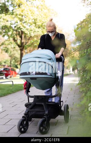 Besorgte junge Mutter, die auf einer leeren Straße mit Kinderwagen in medizinischen Masken geht, um sie vor dem Corona-Virus zu schützen. Soziale Distanzierung während der Corona Stockfoto