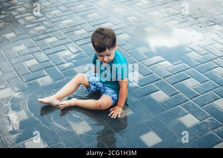 Foto von einem kaukasischen Jungen in blauer Kleidung Spielen auf dem Boden im Wasser im Hinterhof bei Zu Hause Stockfoto