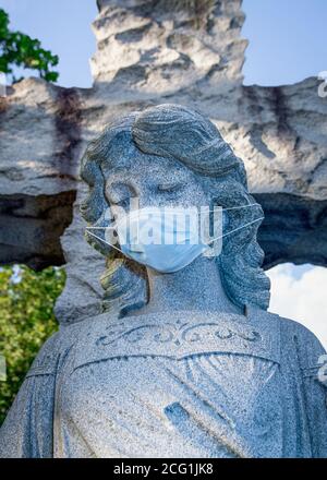 Nahaufnahme einer Friedhofsengelstatue mit einem chirurgischen Eingriff Gesichtsmaske Stockfoto