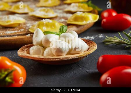 Leckere Ravioli mit Mehl, Kirschtomaten, Sonnenblumenöl und Basilikum auf dunklem Grund. Der Prozess der Herstellung von italienischen Ravioli. Seitenansicht. Stockfoto