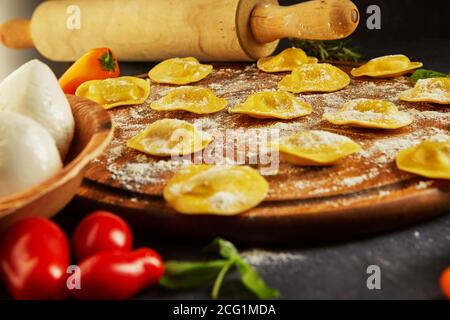 Leckere Ravioli mit Mehl, Kirschtomaten, Sonnenblumenöl und Basilikum auf dunklem Grund. Der Prozess der Herstellung von italienischen Ravioli. Seitenansicht. Stockfoto