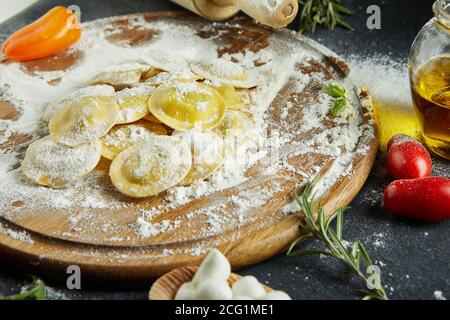 Leckere Ravioli mit Mehl, Kirschtomaten, Sonnenblumenöl und Basilikum auf dunklem Grund. Der Prozess der Herstellung von italienischen Ravioli. Stockfoto