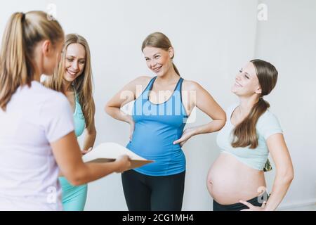 Die Gruppe der schwangeren Frauen in den Sportuniformen kommunizieren mit dem Trainer Im hellen Studio Stockfoto