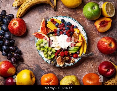 Verschiedene geschnittene Früchte auf Vintage-Teller. Mango, Kiwi-Früchte, Feigen, Trauben, Bananen, Himbeeren und Heidelbeeren mit Joghurt und Müsli. Stockfoto