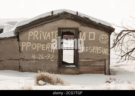 Ein "no Trespassing" Zeichen falsch geschrieben auf den Ruinen einer alten quadratischen Holzhütte im Schnee in der Geisterstadt Cisco, Utah. Stockfoto