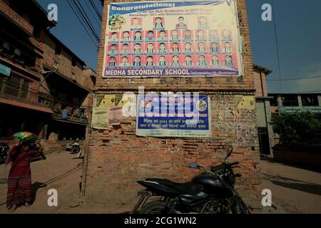 Eine Frau, die auf einer Straße in der Nähe eines Abschlussplakats auf dem Vorhof eines Gymnasiums in Bhaktapur, Nepal, läuft. Stockfoto