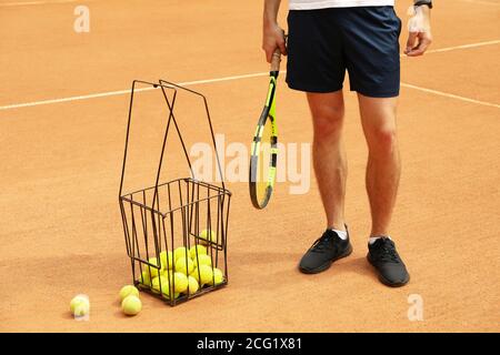 Mann halten Schläger auf Sandplatz mit Korb von Tennis Bälle Stockfoto