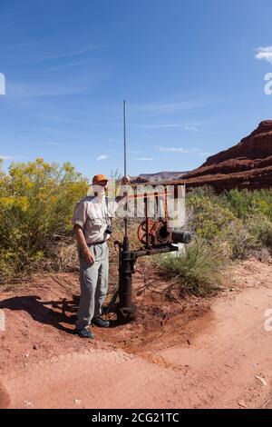 Ein flacher Ölbrunnen mit einem sehr kleinen Pumpenheber im Südosten Utahs. Ein Mann steht neben dem Pumpenheber zur Größenreferenz. Stockfoto