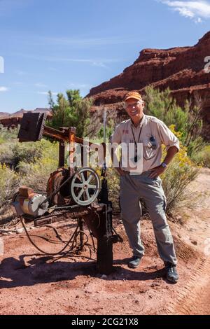 Ein flacher Ölbrunnen mit einem sehr kleinen Pumpenheber im Südosten Utahs. Ein Mann steht neben dem Pumpenheber zur Größenreferenz. Stockfoto