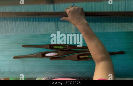 Frau, die an einer Webermaschine für Webhandmaterial arbeitet. Textilweberei. Weberei mit traditionellen Handwedeln auf Baumwollsträngen. Textil Stockfoto