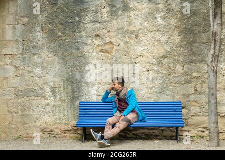 Junger romantischer gutaussehender Mann sitzt allein auf der Bank vor Alte Festung Steinmauer und warten auf Datierung Stockfoto