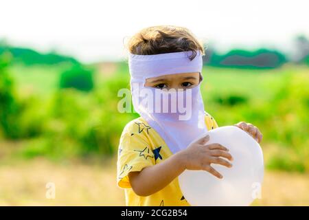 Ein kleines Kind mit weiß geschwollenem Ballon in beiden Händen Und tragen Sie hausgemachte Gesichtsmaske, die vor der schützt Verbreitung von Coronaviren oder COVID-19-Diseas Stockfoto