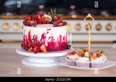 Große schöne rote Samtkuchen, mit Blumen und Beeren auf der Oberseite. Leckere süße Muffins mit Sahne, verziert mit Erdbeeren und Heidelbeeren. Stockfoto