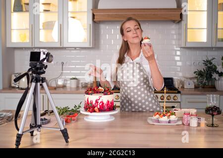 Blogger Konditor macht eine Video-Lektion über das Kochen eines Kuchens, junge Frau in einer Schürze zu Hause in der Küche. Online-Übertragung. Stockfoto