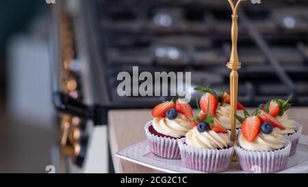 Leckere süße Muffins mit Sahne, verziert mit Erdbeeren und Heidelbeeren. Cupcakes auf dem Küchentisch. Stockfoto