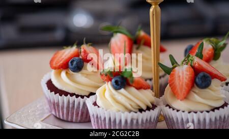 Leckere süße Muffins mit Sahne, verziert mit Erdbeeren und Heidelbeeren. Cupcakes auf dem Küchentisch. Stockfoto