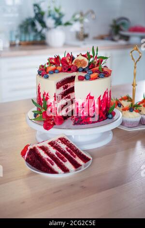 Große schöne rote Samtkuchen, mit Blumen und Beeren auf der Oberseite. Scheibe auf einem Teller, Dessert. Kuchen und Muffins, süße Urlaubssnacks. Stockfoto