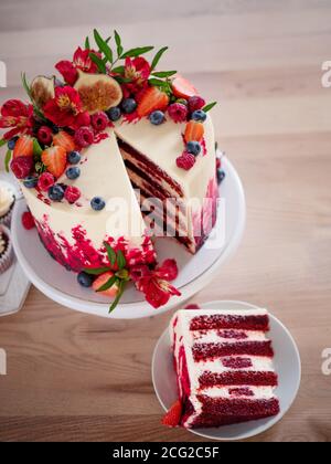 Große schöne rote Samtkuchen, mit Blumen und Beeren auf der Oberseite. Scheibe auf einem Teller, Dessert. Kuchen und Muffins, süße Urlaubssnacks. Stockfoto