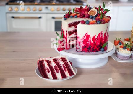 Große schöne rote Samtkuchen, mit Blumen und Beeren auf der Oberseite. Scheibe auf einem Teller, Dessert. Kuchen und Muffins, süße Urlaubssnacks. Stockfoto