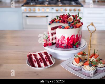 Große schöne rote Samtkuchen, mit Blumen und Beeren auf der Oberseite. Scheibe auf einem Teller, Dessert. Kuchen und Muffins, süße Urlaubssnacks. Stockfoto