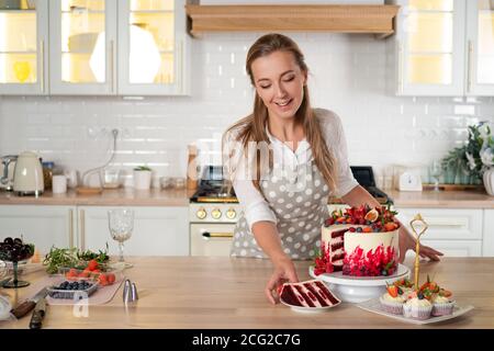 Konditor in der Küche macht Desserts, Kuchen und Muffins. Kochen zu Hause. Köstliche und schöne hausgemachte Kuchen, Gebäck Rezepte. Eine junge Frau. Stockfoto