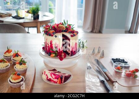 Große schöne rote Samtkuchen, mit Blumen und Beeren auf der Oberseite. Scheibe auf einem Teller, Dessert. Kuchen und Muffins, Kochen zu Hause. Stockfoto