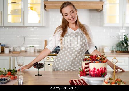 Konditor in der Küche macht Desserts, Kuchen und Muffins. Kochen zu Hause. Köstliche und schöne hausgemachte Kuchen, Gebäck Rezepte. Eine junge Frau. Stockfoto