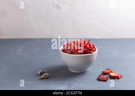 Sonnengetrocknete Tomaten in einer weißen Schüssel mit ein paar Kapern und Knoblauch auf grauem Hintergrund. Speicherplatz kopieren. Horizontale Ausrichtung. Stockfoto