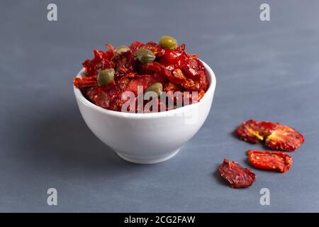 Sonnengetrocknete Tomaten in einer weißen Schüssel mit ein paar Kapern auf grauem Hintergrund. Speicherplatz kopieren. Horizontale Ausrichtung. Stockfoto