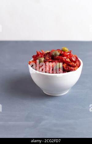 Sonnengetrocknete Tomaten in einer weißen Schüssel mit ein paar Kapern auf grauem Hintergrund. Speicherplatz kopieren. Vertikale Ausrichtung. Stockfoto