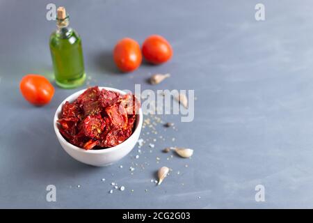 Sonnengetrocknete Tomaten in einer weißen Schüssel mit Gewürzen, Kapern und Olivenöl auf grauem Hintergrund. Speicherplatz kopieren. Selektiver Fokus. Stockfoto