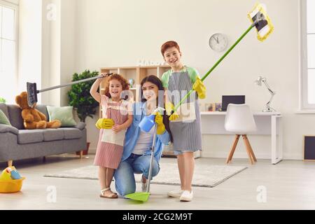 Glückliche Mutter und Kinder mit Bodenmopps und Kehrschaufel lächeln Und nach einem großen Clear-out auf die Kamera schauen Stockfoto