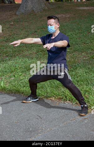 Ein fit junger asiatischer Amerikaner hält diese Pose für einige Minuten, bevor er einen Übungsspaziergang in einem Park in Flushing, Queens, New York City beginnt. Stockfoto