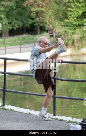 Ein flink flexibler Senioren berührt seine Zehen auf unkonventionelle Weise, während er sich für einen Übungsspaziergang aufwärmt. In einem Park in Queens, New York City. Stockfoto