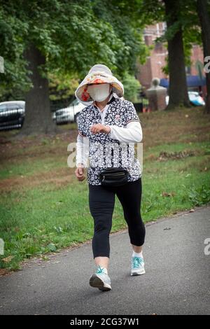 Eine asiatisch-amerikanische Frau, deren Gesicht fast vollständig von ihrer Maske bedeckt ist. Auf einem flotten Übungsspaziergang im Kissenal Park, Flushing, Queens, New York. Stockfoto