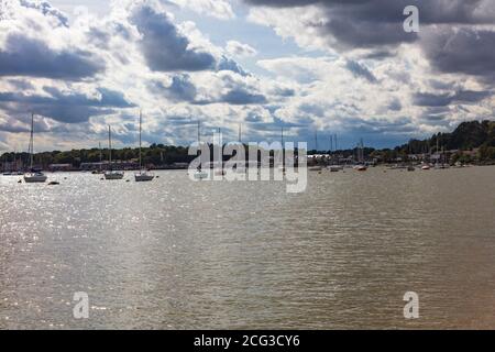 Am späten Nachmittag bricht die Sonne durch die Sturmwolken und funkelt auf dem Wasser unter den festgetäuten Yachten in Upnor am Fluss Medway, Kent, Großbritannien Stockfoto