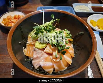 Sake-don oder Salmon Donburi, japanische traditionelle Reisschüssel mit Stapel von rohem Lachsbauch, Wasabi und Sprossen gekrönt. Gewürzt mit Sojasauce. Stockfoto