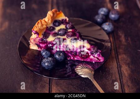 Rustikaler Shortbread-Kuchen mit Heidelbeeren in saurer Sahne Füllung auf einem Holzhintergrund mit Stück abgeschnitten auf Untertasse und Löffel. Stockfoto