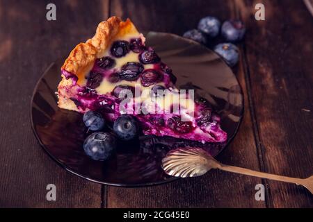 Stück auf Untertasse abgeschnitten Rustikale Shortbread Pie mit Heidelbeeren in saurer Sahne Füllung auf einem hölzernen Hintergrund mit Löffel. Stockfoto