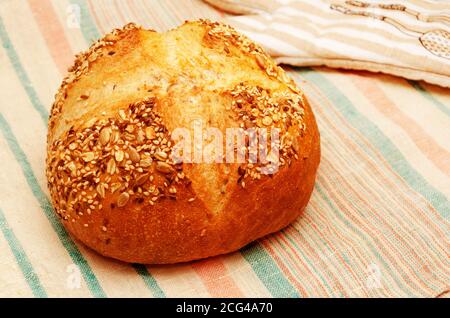 Frisch gebackenes goldenes Mehrkornbrot. Runder Laib mit Knäckebrot bestreut mit Samen von Flachs, Sesam, Sonnenblume. Hausbackkonzept. Gesunde Ernährung Stockfoto