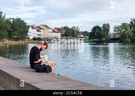 Ein Mann liest ein Buch am Ufer des Flusses Swisloch. Trinity Vorort. Stockfoto