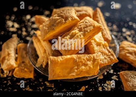 Klassisches Jeera Khari oder Blätterteig in einer Glasplatte auf einer schwarzen Oberfläche. Ein Schuss frisch gebackener Blätterteig-Snack auf einem Servierteller. Stockfoto