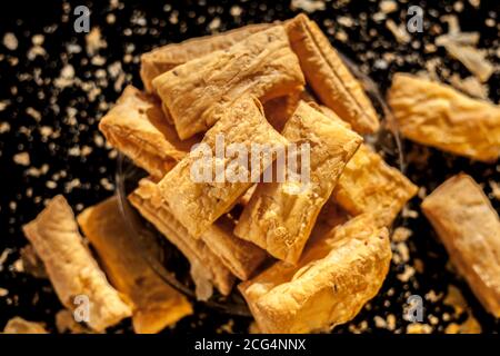 Klassisches Jeera Khari oder Blätterteig in einer Glasplatte auf einer schwarzen Oberfläche. Ein Schuss frisch gebackener Blätterteig-Snack auf einem Servierteller. Stockfoto