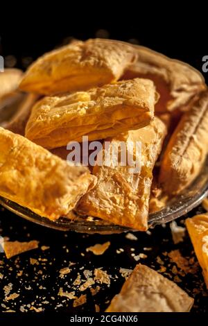 Klassisches Jeera Khari oder Blätterteig in einer Glasplatte auf einer schwarzen Oberfläche. Ein Schuss frisch gebackener Blätterteig-Snack auf einem Servierteller. Stockfoto