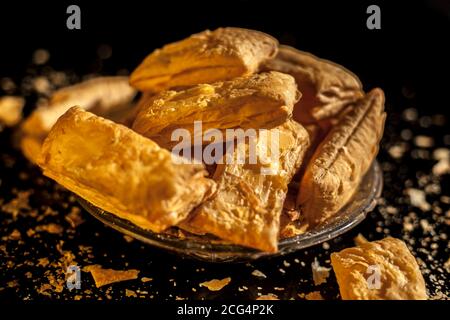 Klassisches Jeera Khari oder Blätterteig in einer Glasplatte auf einer schwarzen Oberfläche. Ein Schuss frisch gebackener Blätterteig-Snack auf einem Servierteller. Stockfoto